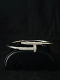 A Close-up view silver cuff bracelet with pave-set diamond forming a stylized T-shape, displayed on a black stand
