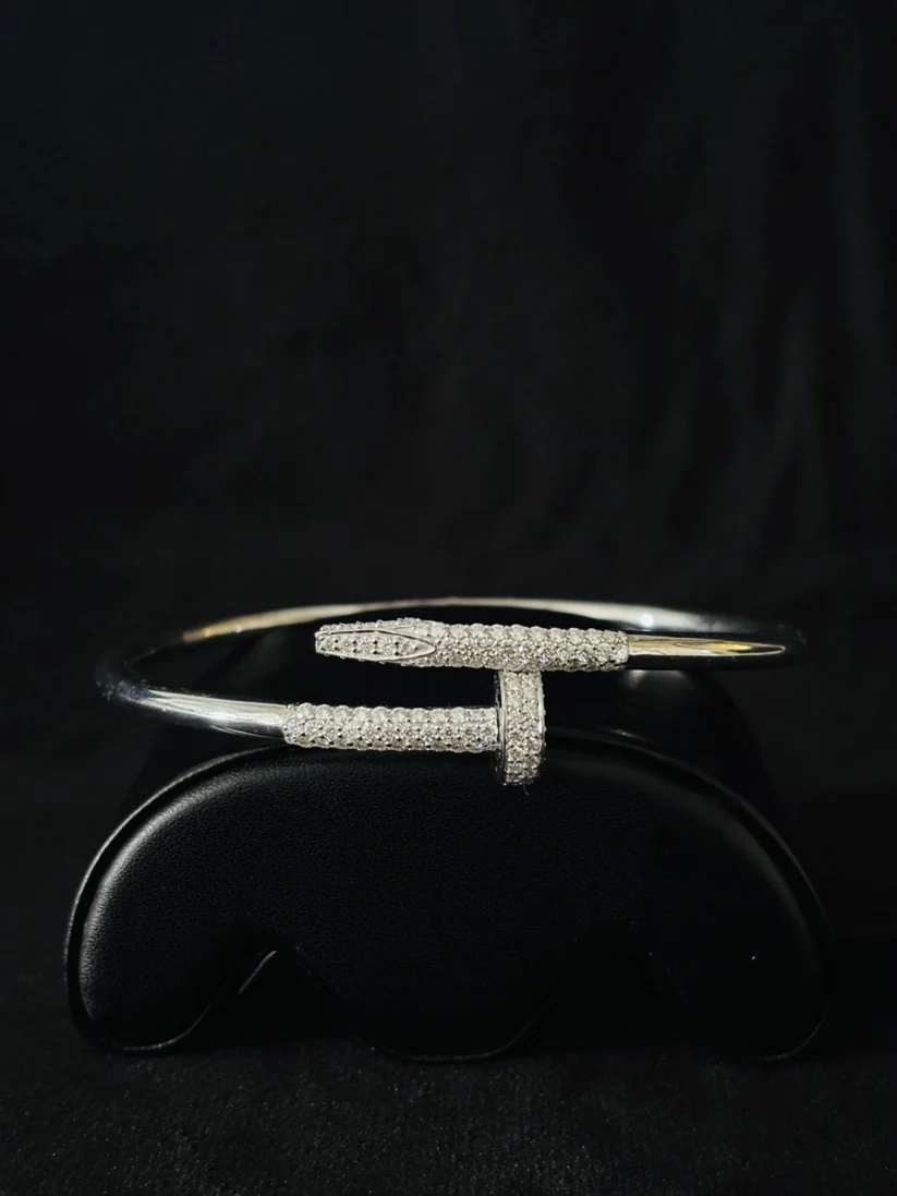 A Close-up view silver cuff bracelet with pave-set diamond forming a stylized T-shape, displayed on a black stand