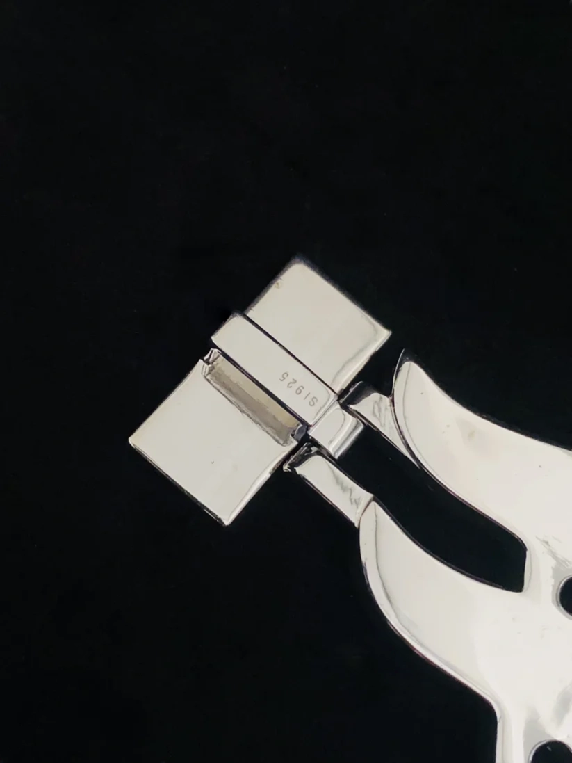 Close-up of a polished silver metal fold-over clasp on a luxury handbag strap against a black background.