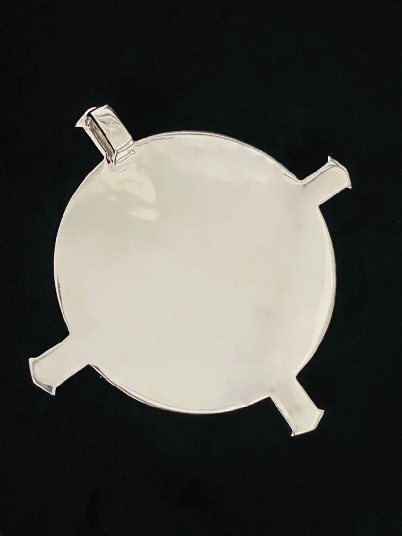 Polished silver round pendant with four decorative extensions against a black background.