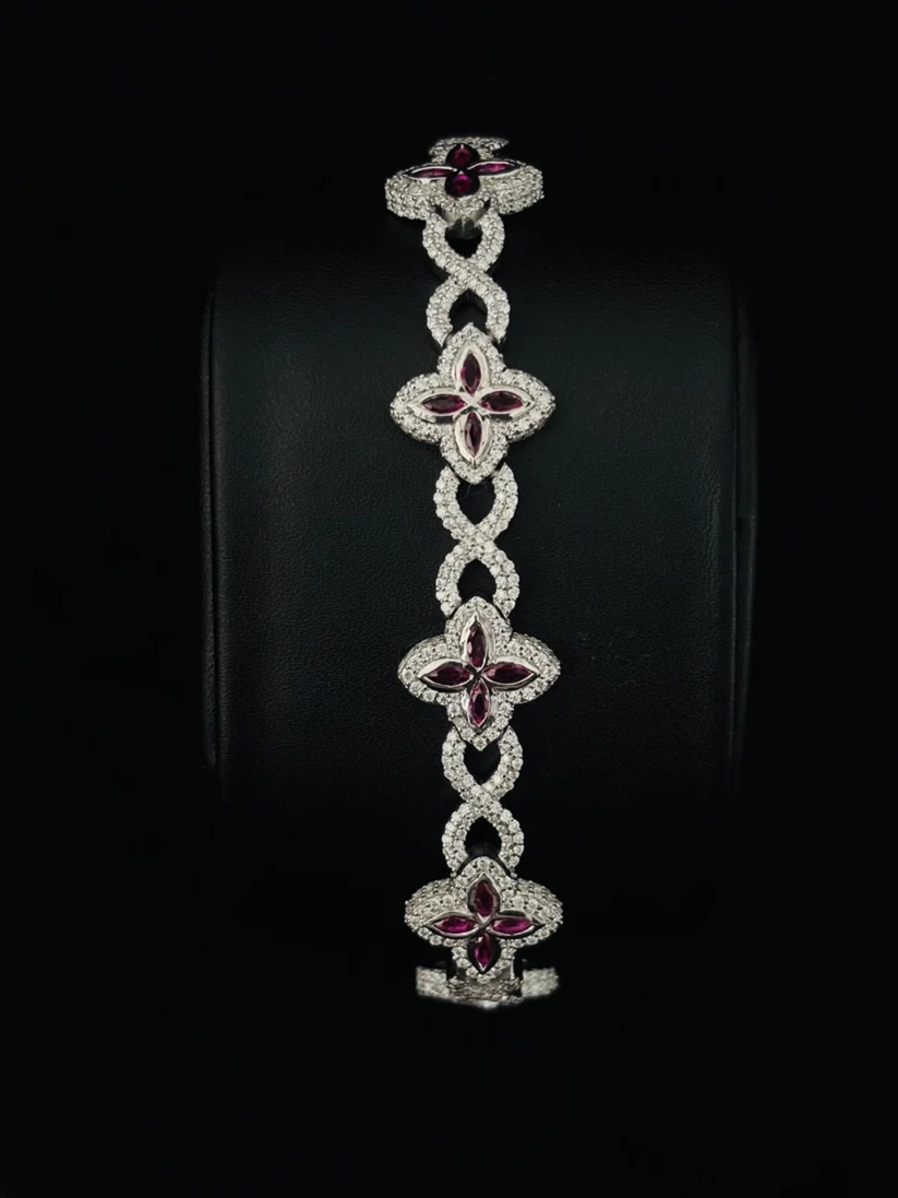 A luxury bracelet featuring five interlocking clover motifs, each adorned with sparkling diamond and deep red gemstones