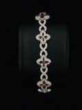 A luxury bracelet featuring five interlocking clover motifs, each adorned with sparkling diamond and deep red gemstones