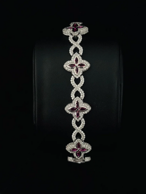 A luxury bracelet featuring five interlocking clover motifs, each adorned with sparkling diamond and deep red gemstones
