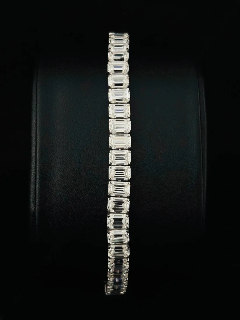 A close-up view slim tennis bracelet featuring a single vertical row of emerald-cut diamond in a silver