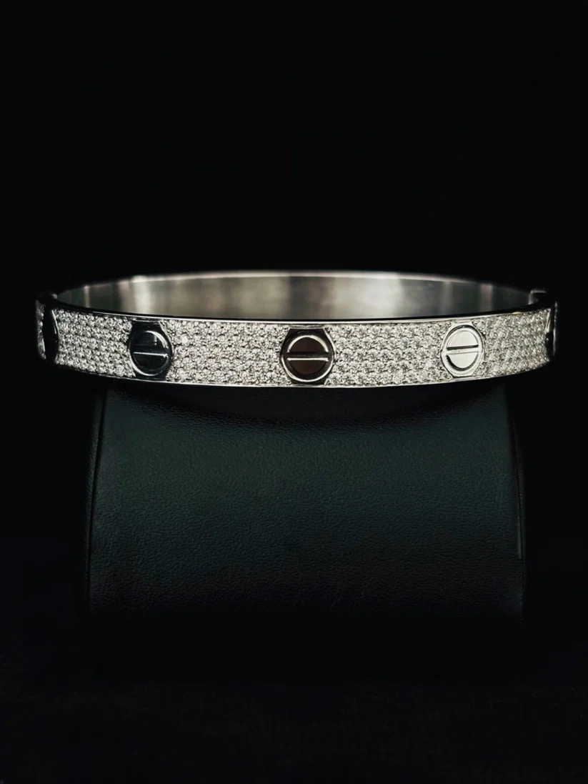 A close-up view silver bangle bracelet with a pave-set diamond band and three screw-head accents