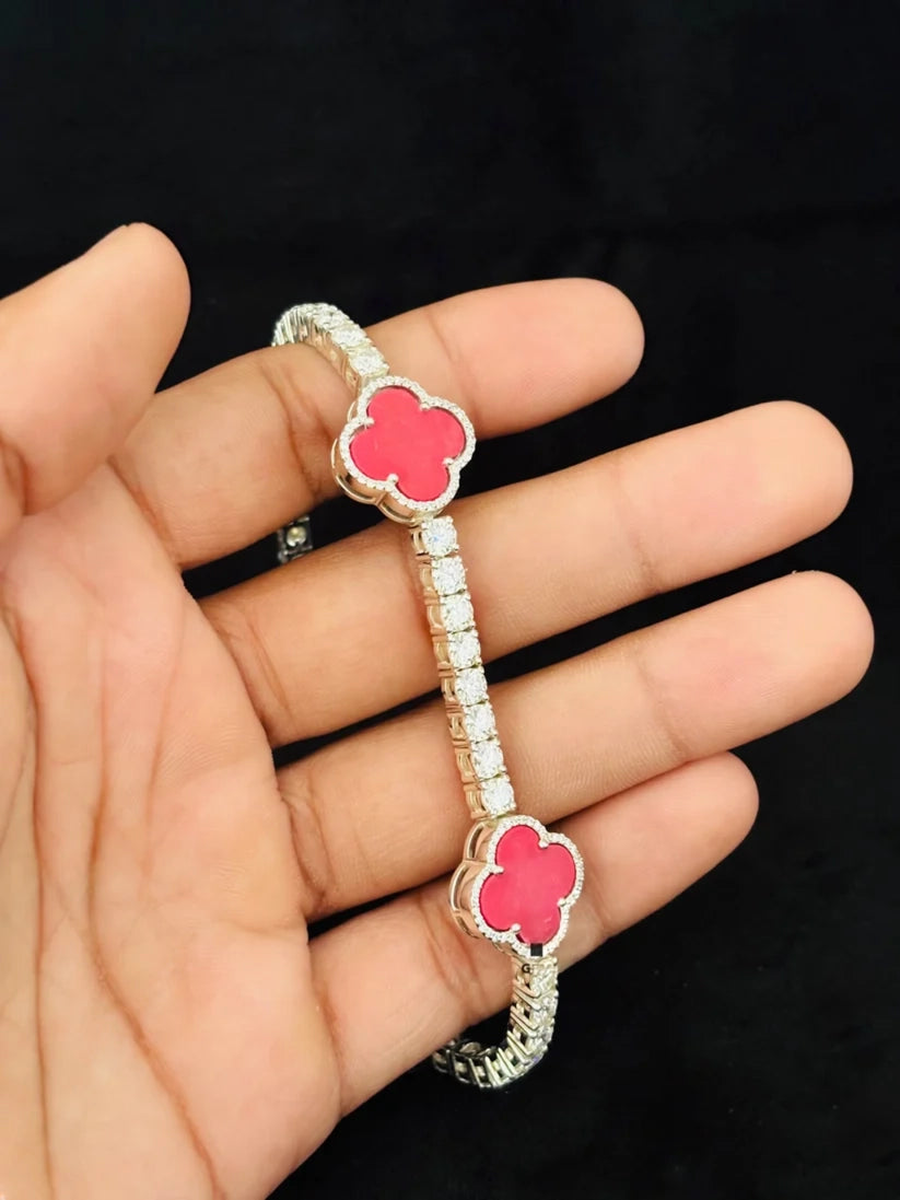 A hand holding a silver four-leaf clover tennis bracelet with red enamel stations