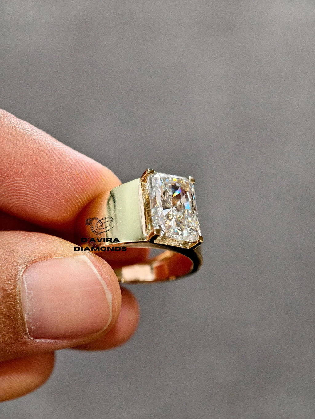 A close-up of a hand holding a gold ring with a radiant cut diamond ring