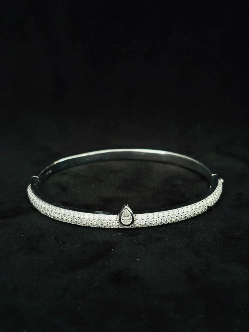 Silver pave diamond bangle bracelet featuring a central teardrop shaped charm on a black background