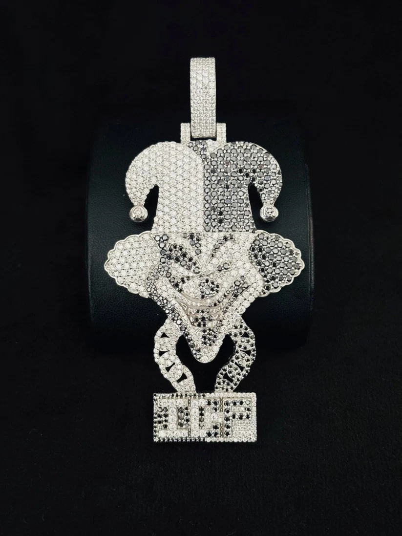 A large, ornate silver jester pendant covered in diamond, displayed on a black cylindrical stand