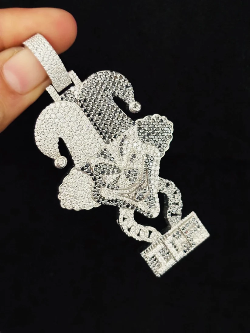 A close-up of a silver jester pendant heavily encrusted with clear rhinestones, held by a hand