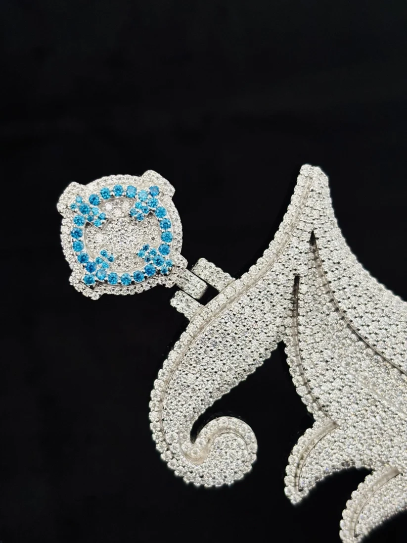 Close up of an iced-out silver custom letter pendant studded with clear and blue diamonds