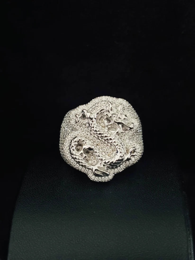 A silver ring featuring an intricate raised dragon motif, displayed on a black ring stand