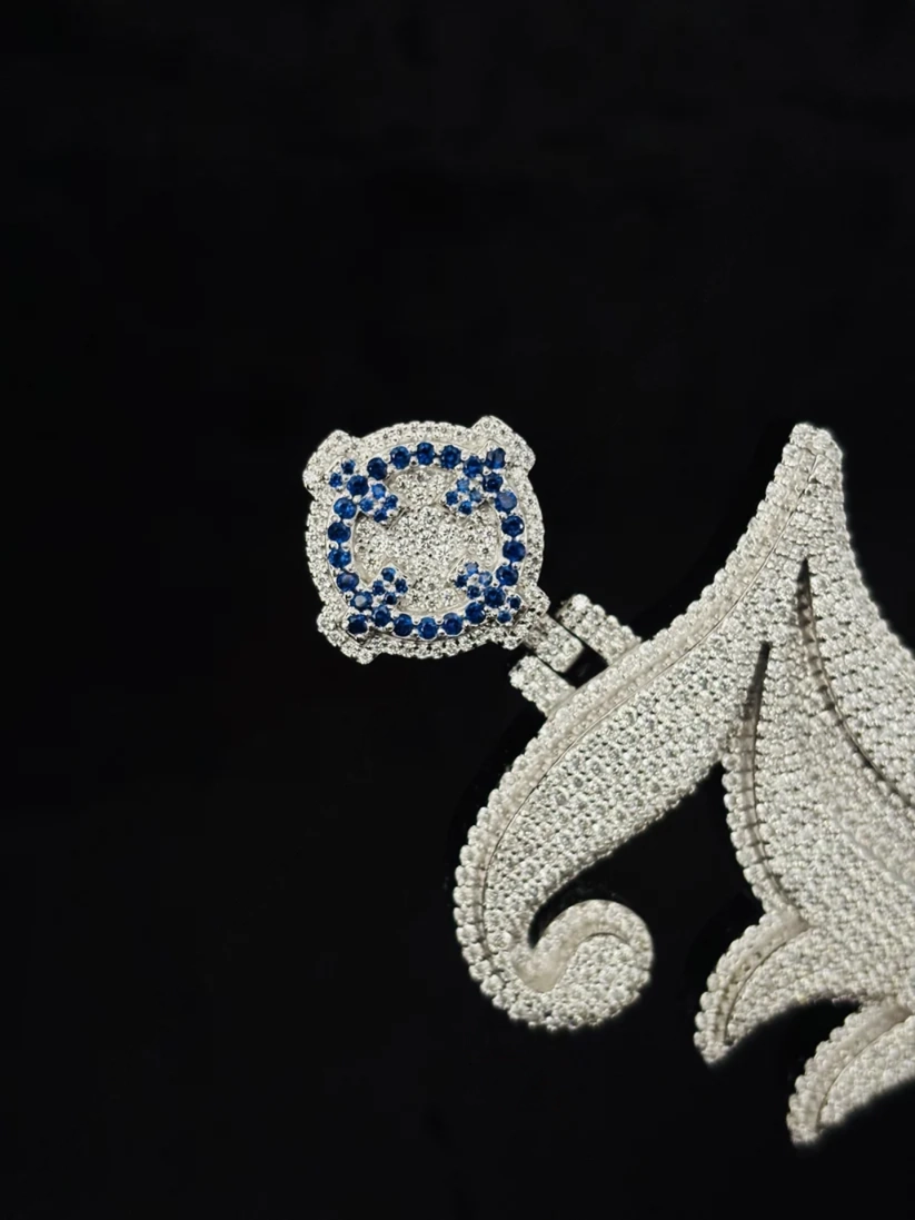 Custom diamond iced out letter J pendant in white gold with blue sapphire accents.
