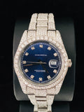 front view Custom diamond encrusted stainless steel watch with blue dial and date window on a black display stand
