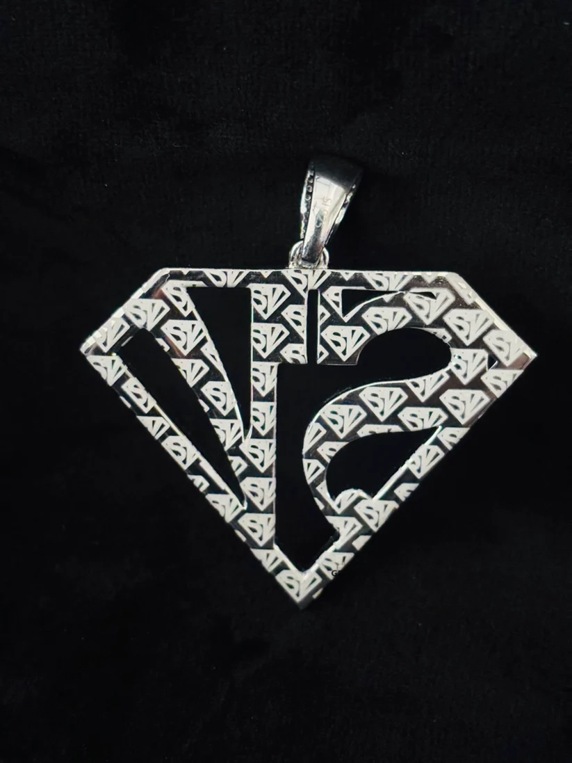 back view A silver pendant shaped like a diamond with an intricate geometric pattern and a stylized 'VS' monogram 