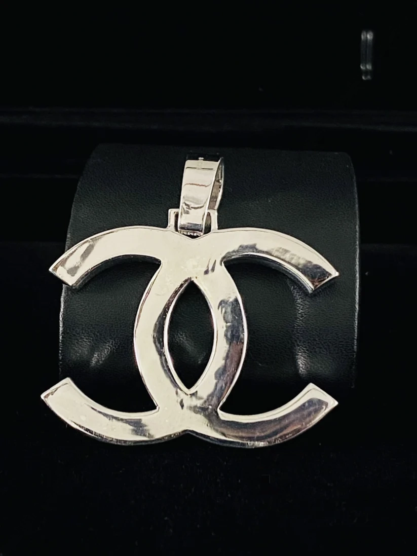 Silver interlocking CC logo pendant necklace on a black display stand, luxury fashion jewelry.