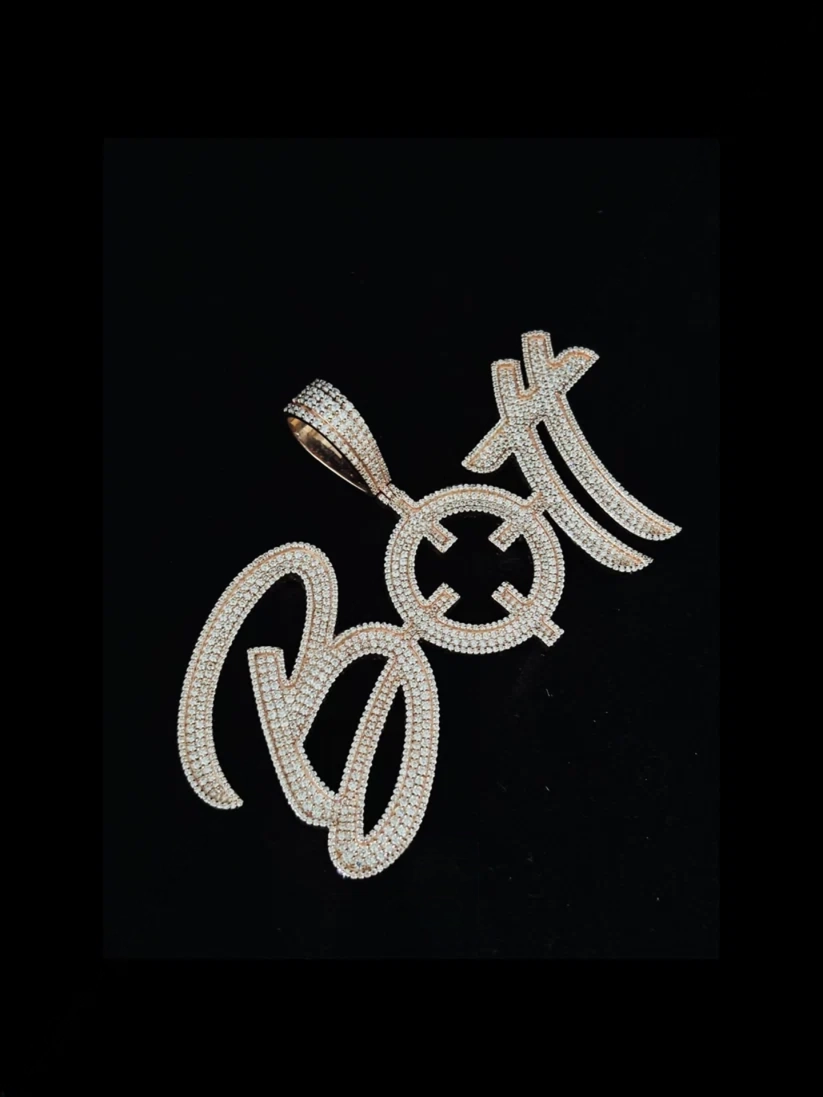 Silver cursive letter BOTT pendant necklace studded with diamonds against a black background.