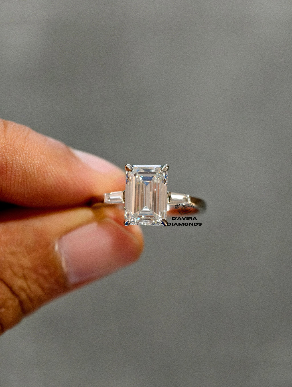 Emerald cut lab diamond ring with tapered baguette side stones held by a hand