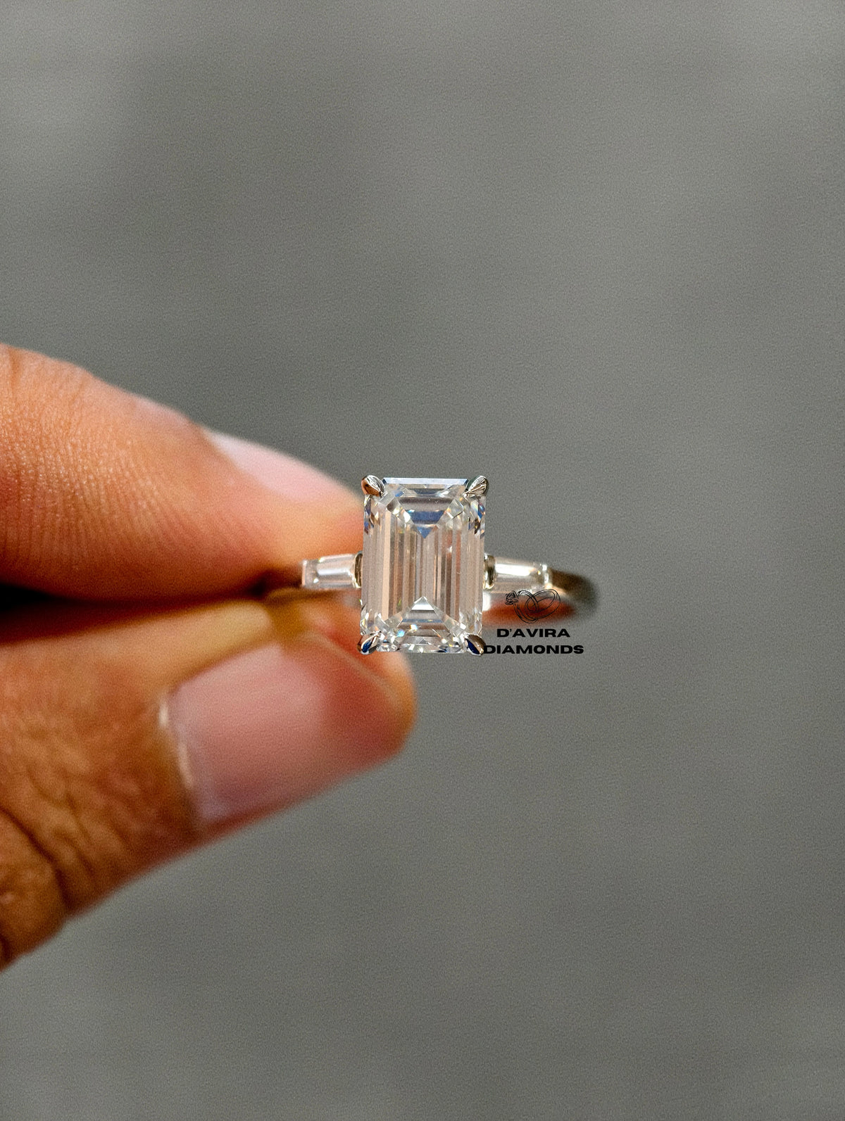 Emerald cut lab diamond ring with tapered baguette side stones held by a hand