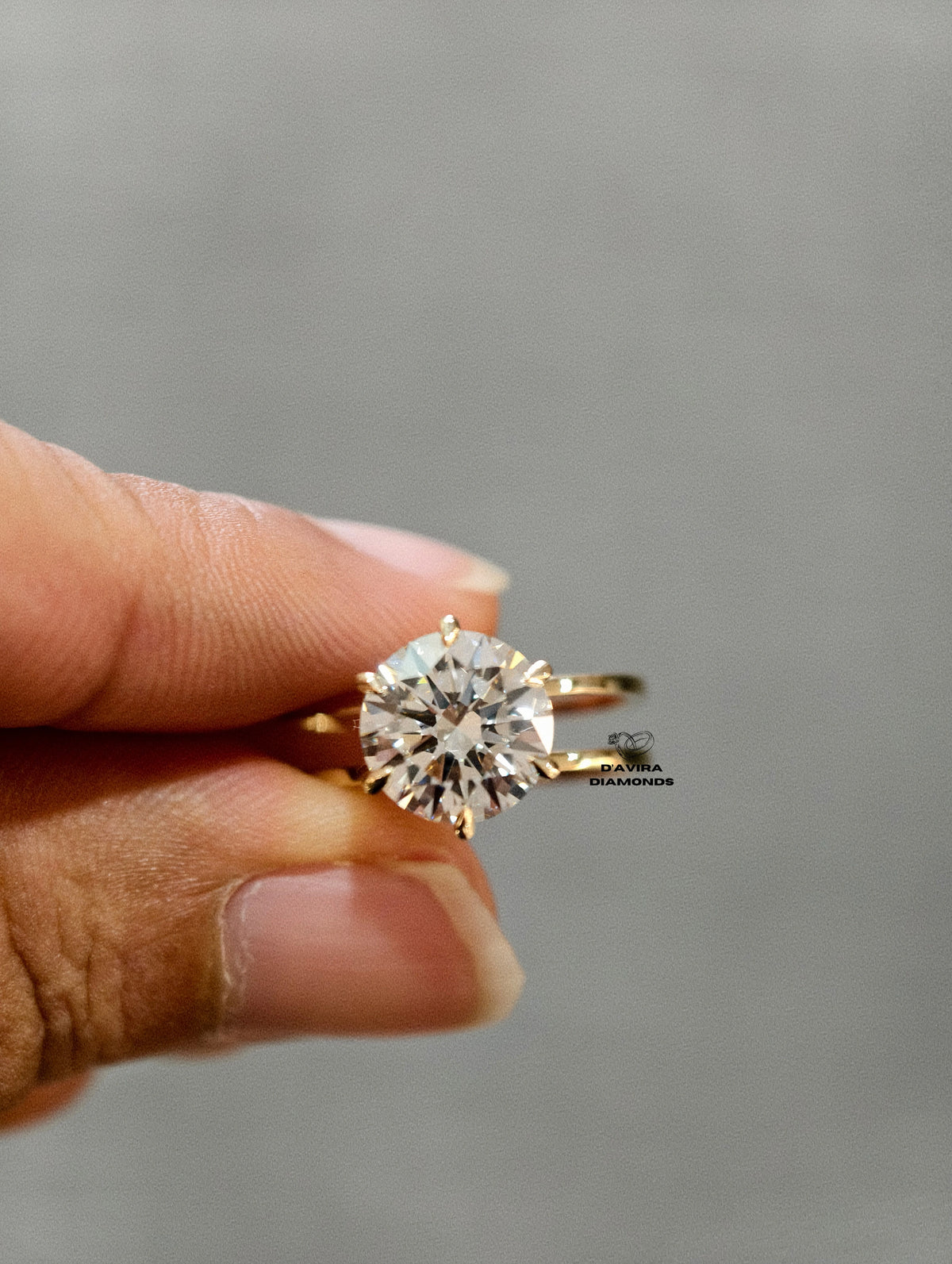A close-up of a hand holding a yellow gold solitaire engagement ring