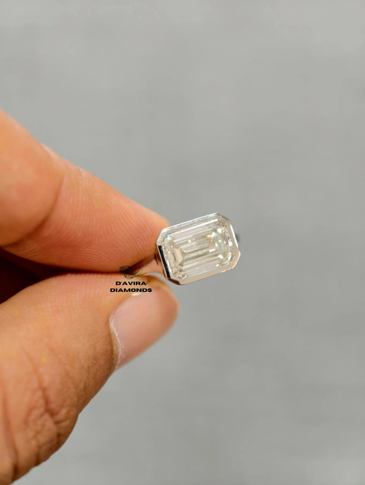 A hand holding an emerald-cut diamond engagement ring