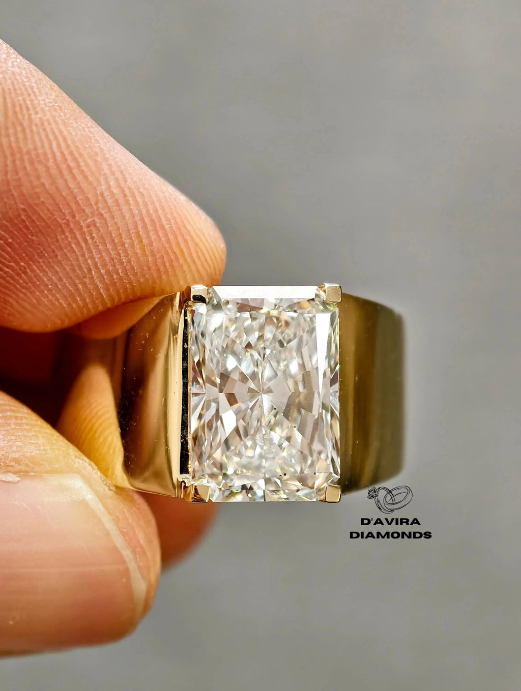 close-up Radiant cut diamond men's ring in wide yellow gold band.