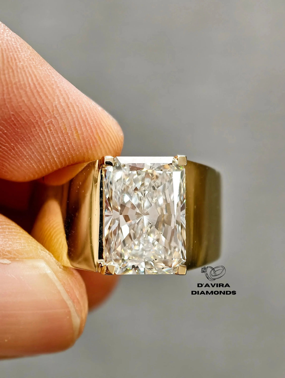 close-up Radiant cut diamond men's ring in wide yellow gold band.