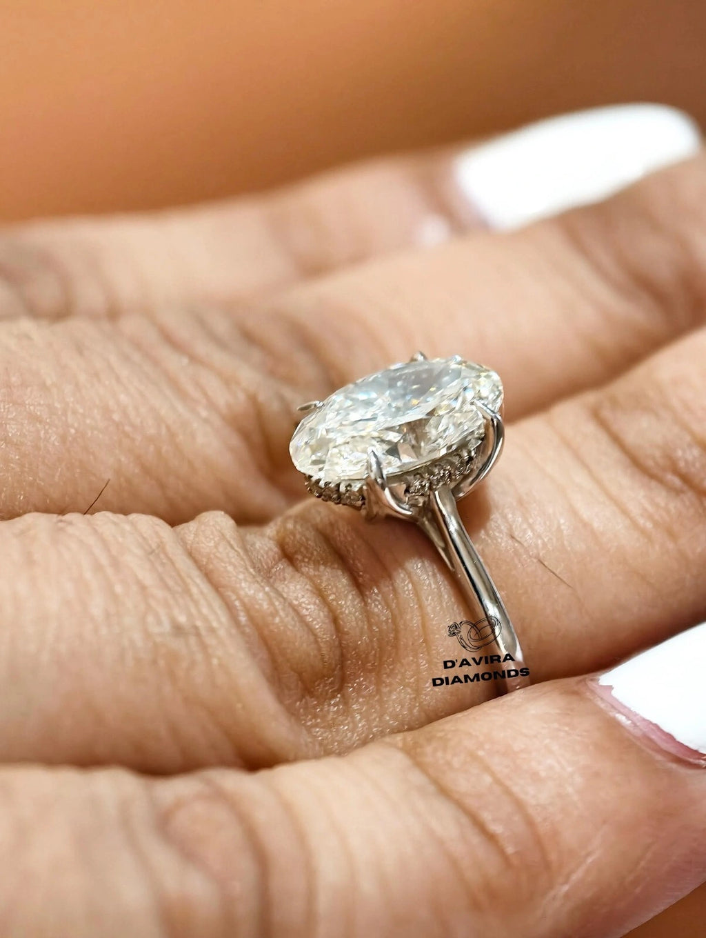 Oval cut diamond engagement ring with hidden halo on finger.