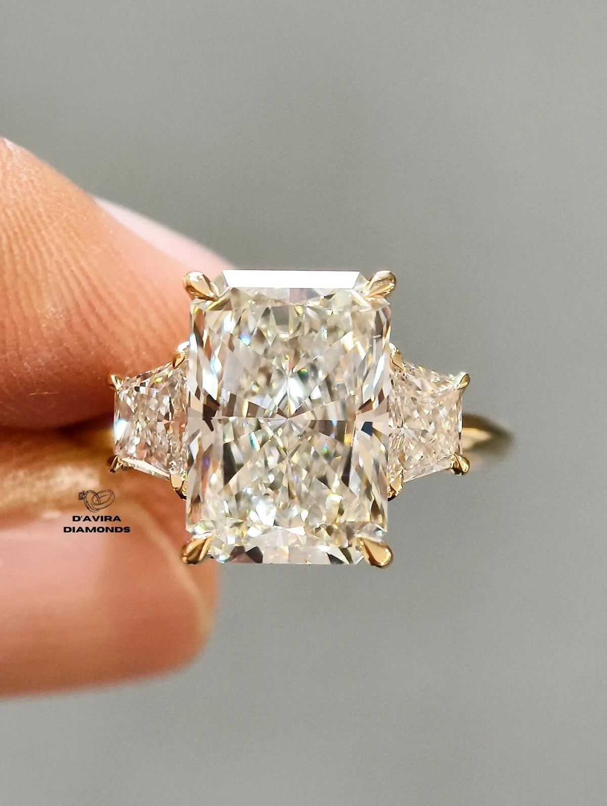 Radiant cut diamond engagement ring with trapezoid side stones in a gold setting held by hand