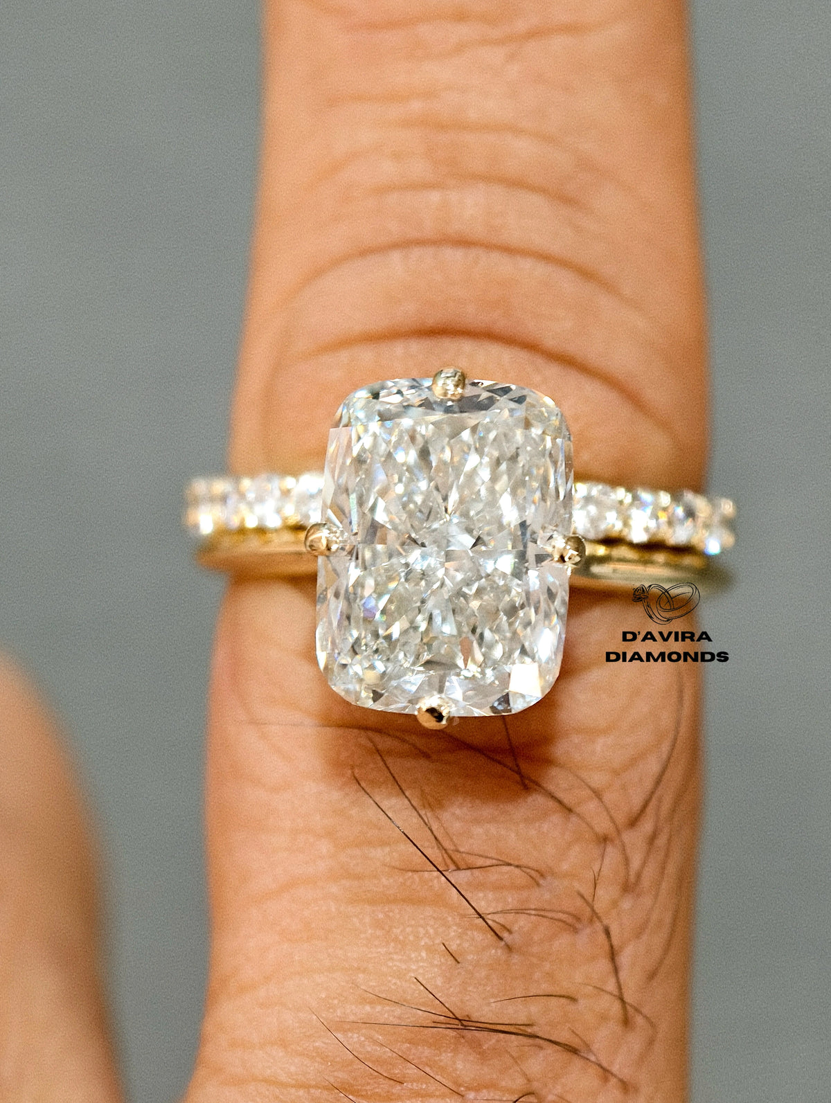 Elongated cushion cut diamond engagement ring with a pave diamond band on a finger