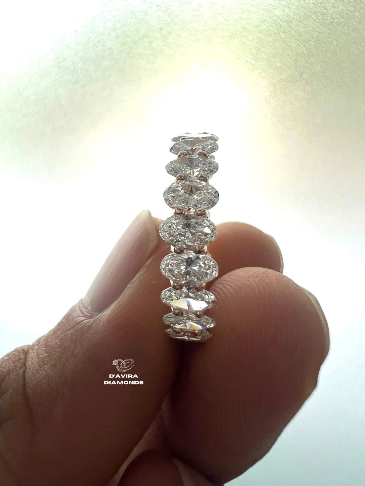 A close-up of a hand holding a eternity ring with round cut diamonds
