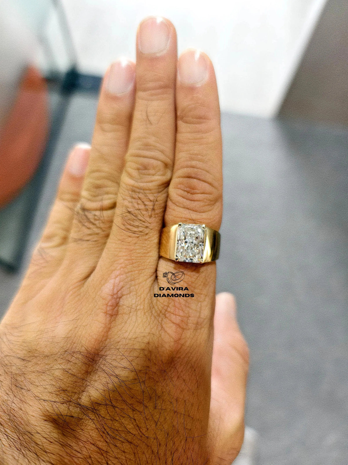 A gold signet ring with a radiant cut diamond on a person ring finger